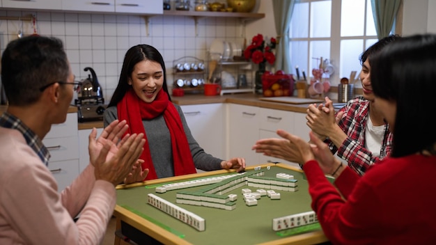 Family members clapping hands for the winning daughter who\
claims a discarded tile and completes her hand while playing\
mahjong game at home on chinese lunar new year\'s eve