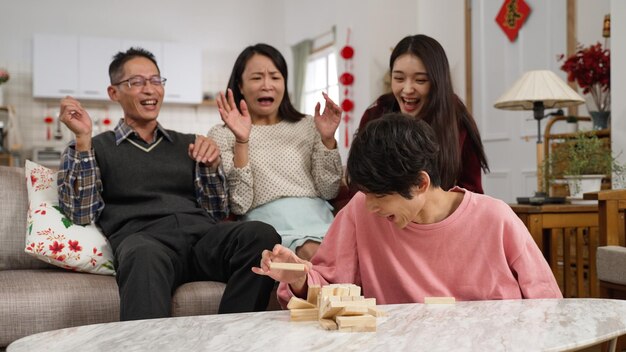 family members and son folding arms and feeling upset as he makes the toy wood blocks tower fall while trying to remove a block. chinese word on door translation: spring