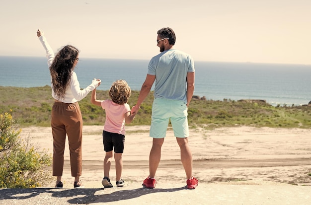 Family of mom dad and child boy looking in future holding hands in summer back view happy family