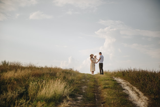 Photo family, mom, dad, daughter are walking on a hill in the field. mom and daughter in yellow identical dresses.