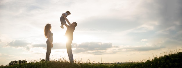 Photo family mom dad and little son walk at sunset silhouettes of parents and toddler child on the background of the sky freedom and an active lifestyle