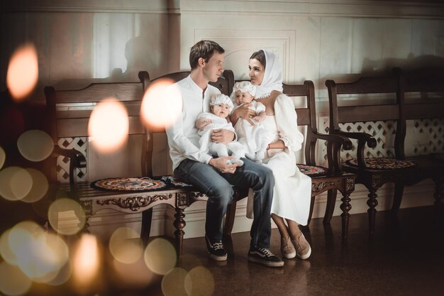 Family mom dad with small twin children in a temple or church\
praying near an icon and candles or came to worship in the russian\
orthodox church baptism of a baby