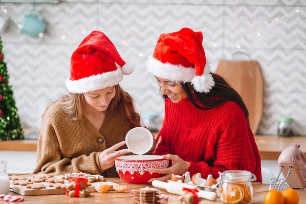 サンタハットのママと娘の家族がキッチンでクリスマスクッキーを準備します