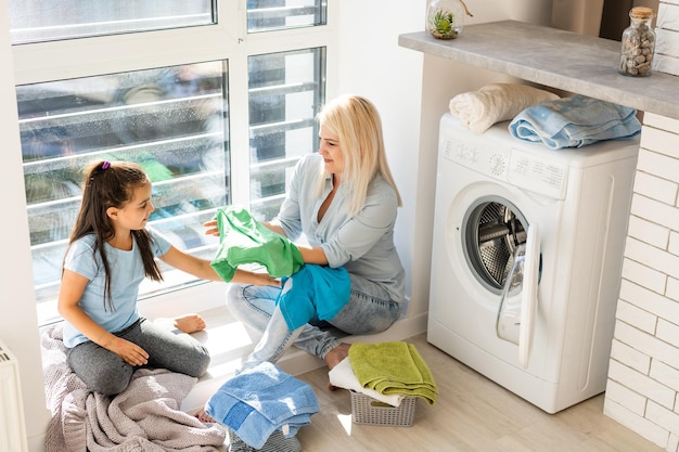 family mother and child girl little helper in laundry room near washing machine and dirty clothes