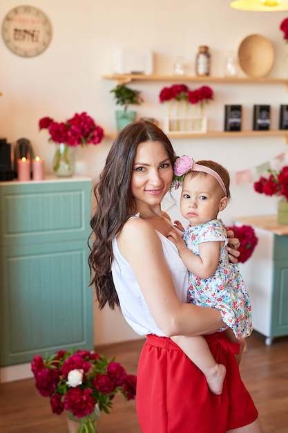 Family mother and daughter with peonies flowers in kitchen at home. Happy mother and baby daughter. Happy family. 