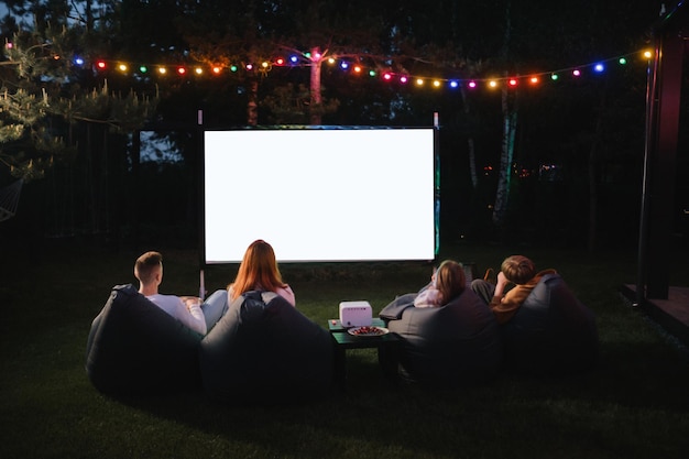 Photo family mother father and children watch a projector movies with popcorn in the evening in the courtyard