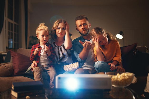 家族の母親の父親と子供たちが家で夕方にポップコーンを使ってプロジェクター テレビの映画を見ている