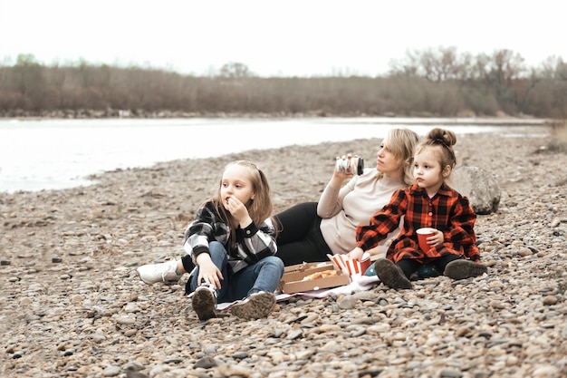 family mother with little daughters on a picnic in nature by the river outside the city