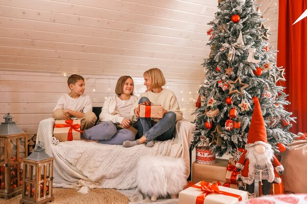 クリスマスイブの家族。キッズオープニングプレゼント。ギフトボックスとクリスマスツリーの下の子供たち。新年の装飾が施された部屋。自宅で居心地の良い暖かい冬の夜。