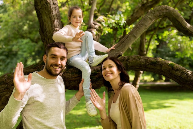 family, parenthood, adoption and people concept - happy mother, father and little girl in summer park waving hands