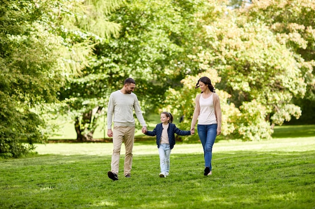 家族、親子関係、養子縁組、人のコンセプト – 幸せな母、父、夏の公園を歩く少女