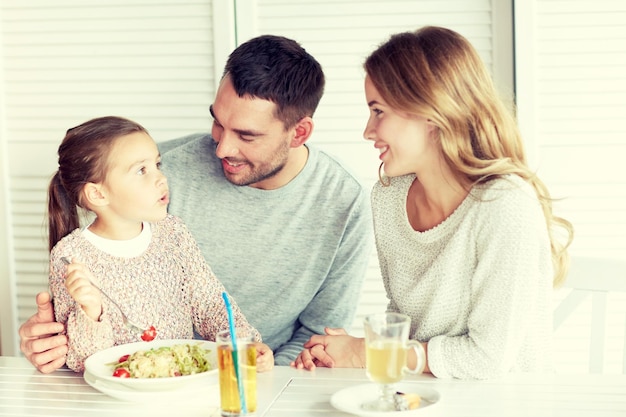 family, parenthood, communication and people concept - happy mother, father and little girl eating pasta for dinner and talking at restaurant or cafe