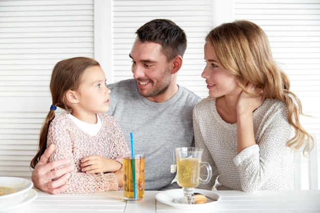 family, parenthood, communication and people concept - happy mother, father and little girl having dinner and talking at restaurant or cafe