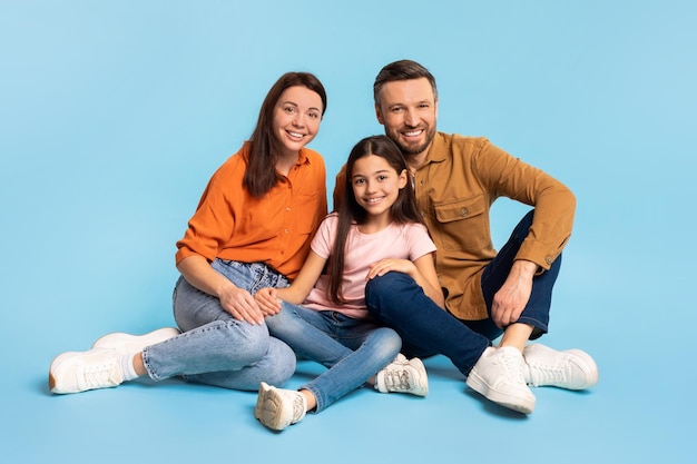 Family of parents and daughter shares hug sitting on floor