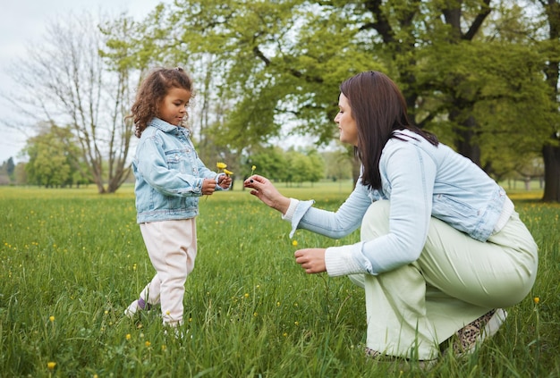 Family park and flower with a mother and girl child bonding together on a grass field during summer or spring Nature love and children with a woman and female kid spending time outdoor on holiday