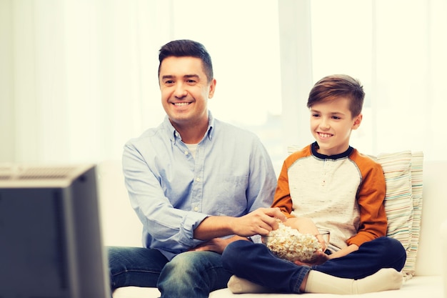 Photo family, people, technology, television and entertainment concept - happy father and son with popcorn watching tv at home