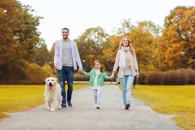 Concetto di famiglia, animale domestico, animale domestico, stagione e persone - famiglia felice con cane labrador retriever che cammina nel parco autunnale