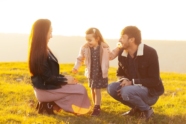 Family photo of parents and little girl having time in park or field on sunset