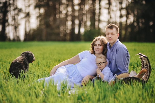 Famiglia a fare un picnic nella foresta. nel prato. cestino da picnic con cibo. il cane corre e vuole giocare. un bambino con gli occhiali. colore blu nei vestiti. per mangiare all'aperto. tempo con la famiglia.