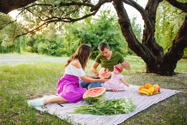 Family at picnic Mother feeding baby girl with watermelon in the garden