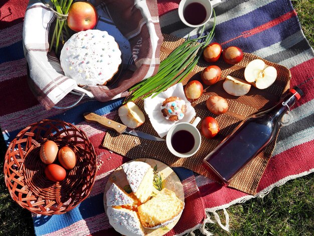 Foto picnic in famiglia con torte pasquali, vino e uova, mangiando l'erba sul prato in natura.