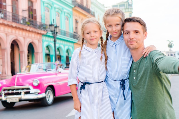 Famiglia nella zona popolare di l'avana vecchia, cuba. ritratto di due bambini e giovani papà all'aperto su una strada dell'avana