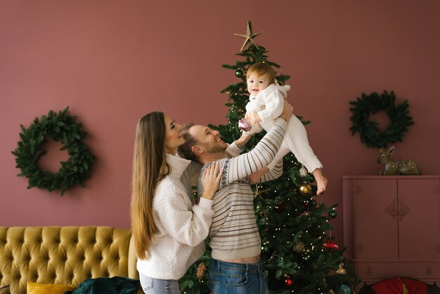 クリスマスツリーの近くに小さな子供を持つスタイリッシュな若い家族の家族の肖像画