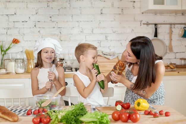 Family prepares lunch in the kitchen. Mom teaches her daughter and son to prepare a Salad of fresh vegetables. Healthy natural food, vitamins for children