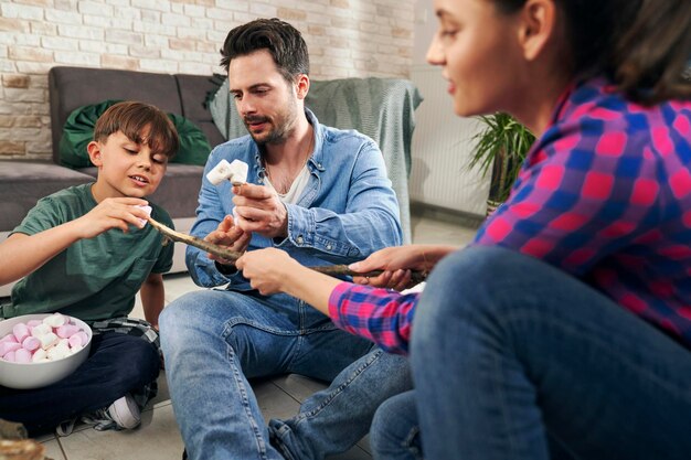 Photo family preparing marshmallows by the fire at home