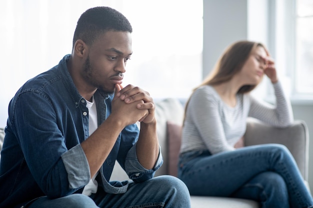 Photo family problems. portrait of upset interracial couple sitting on couch after quarrel, depressed young multicultural spouses suffering relationship crisis, selective focus on sad black man