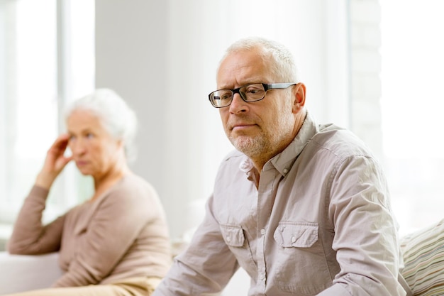 family, relations, age and people concept - senior couple sitting on sofa at home