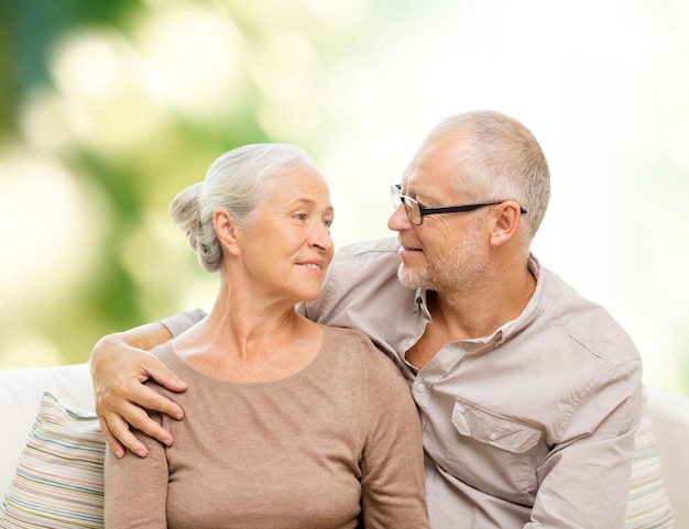 семья, отношения, любовь, возраст и концепция людей - счастливая пожилая пара обнимается и смотрит друг на друга на диване на зеленом фоне