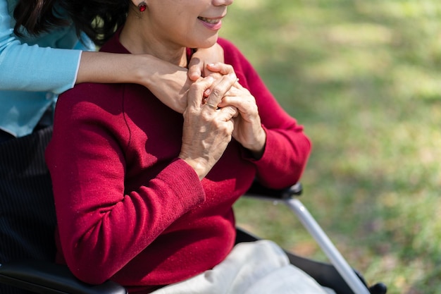 Семейные отношения Азиатская пожилая женщина в инвалидной коляске со счастливой дочерью, держащей сиделку за руку, проводя время вместе