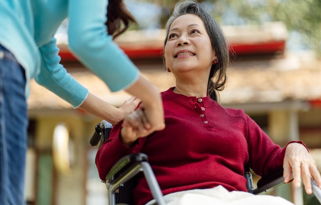 Family relationship Asian senior woman in wheelchair with happy daughter holding caregiver for a hand while spending time together