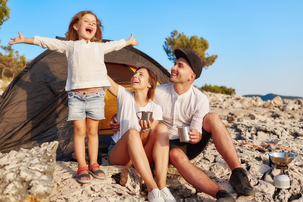 Photo family resting near tent, little girl standing and holding hands up.