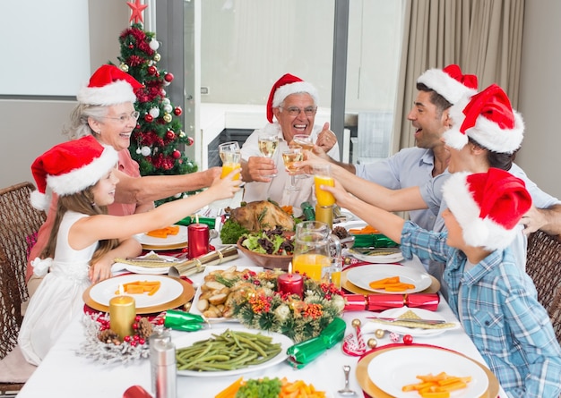 Семья в шляпах santas, поджаривающих бокалы в обеденном столе