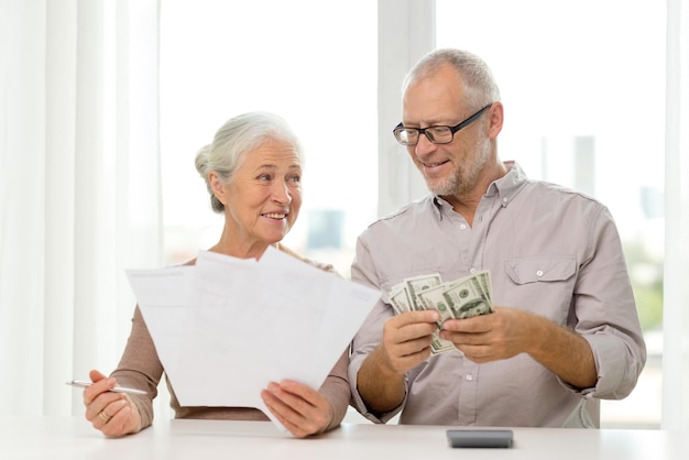 家族、貯蓄、年齢、人々の概念-自宅で書類、お金、電卓を持って笑顔の老夫婦