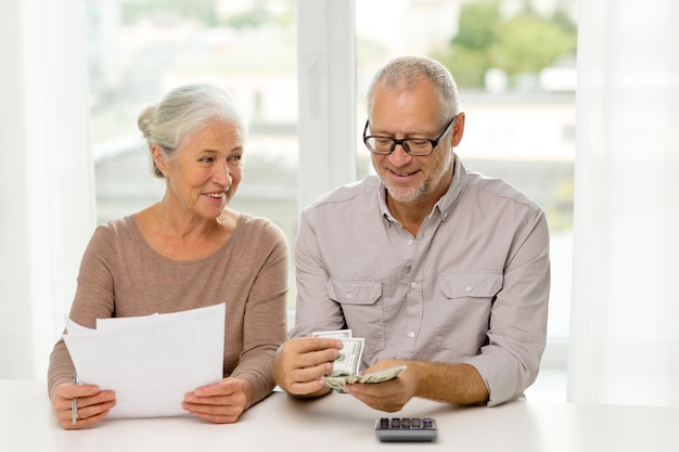 Foto concetto di famiglia, risparmio, età e persone - coppia senior sorridente con documenti, denaro e calcolatrice a casa