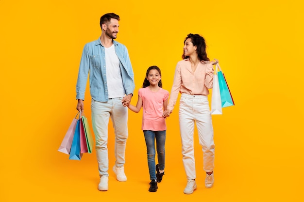 Photo family shopping concept happy caucasian parents and daughter carrying shopper bags yellow background