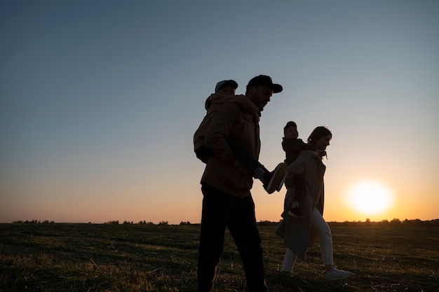 Foto sagome familiari che si divertono al tramonto vista laterale