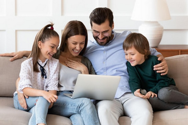 a family sits on a couch with a laptop and a family smiling