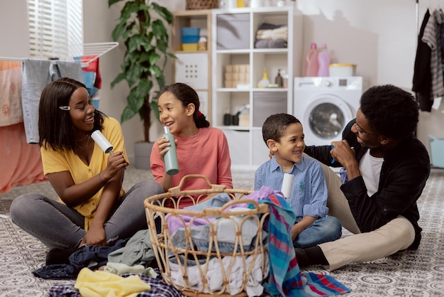 A family sits on the laundry room floor sorting clothes before\
putting them in the washing machine playing together during\
household chores singing to random objects