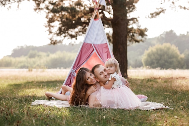 家族座って、ピンクのウィグワムの近くの夏の公園で楽しんで