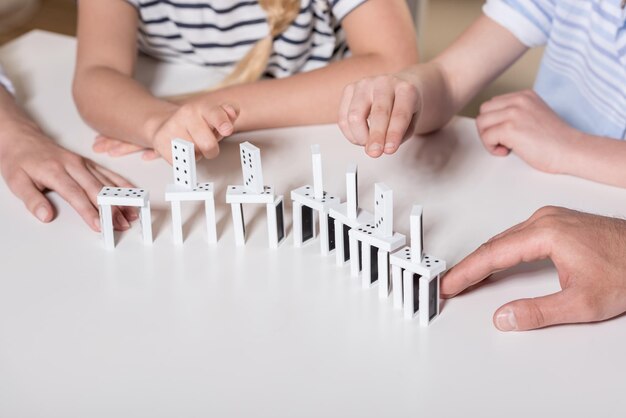 Family sitting at table and playing with domino pieces cropped image