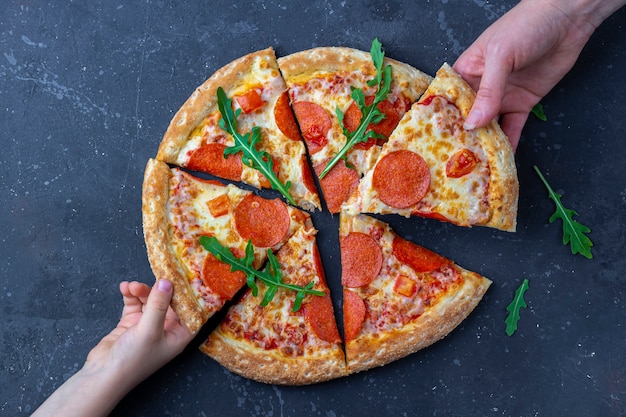 Foto mani della famiglia spuntino, madre e figlio prendendo fette di pizza peperoni.