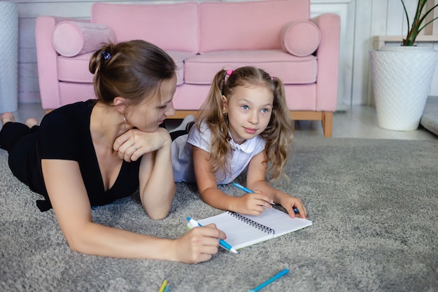 Family spending time together at home. Mom with her daughter draw on the floor. Parental control, lifestyle and kids concept.