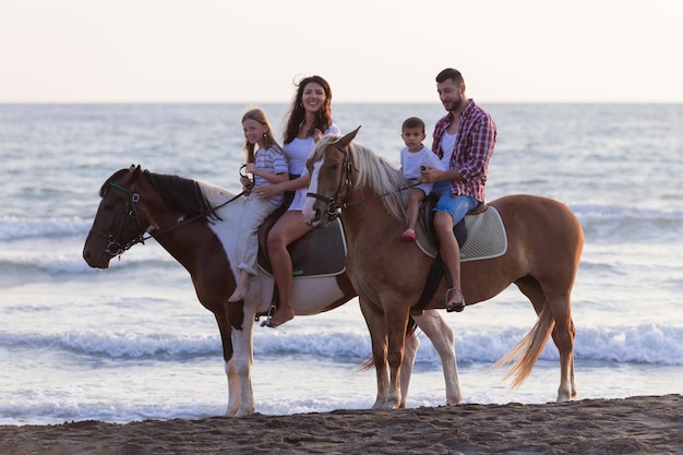 The family spends time with their children while riding horses together on a sandy beach. Selective focus. High quality photo