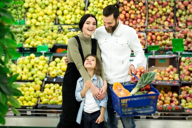 Photo family standing with a full cart in the supermarket in the vegetable department