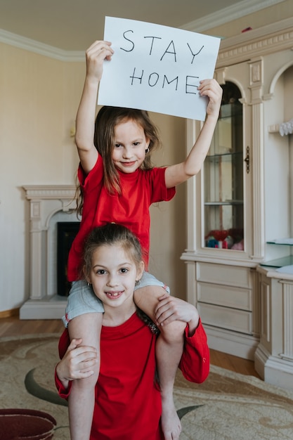 Foto famiglia stare a casa concetto. due ragazze con cartello che dicono di rimanere a casa per la protezione da virus e di prendersi cura della propria salute da covid-19. concetto di quarantena.