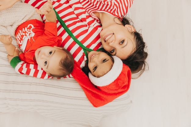 Family in striped pajamas resting at home. Little children are lying on the bed, wearing santa claus hats. A happy family.view from above